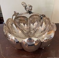 Front view of a reflective silverplate, scalloped bowl with a squirrel on a branch handle accent and floral details.