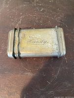 Top view of a small vintage rectangular metal case with rounded edges, marked 'Warming', rubber band around it.