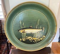 Front view of large green dish with painted fish, showing overall design and surface cracks.