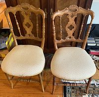 Photo of two vintage chairs with carved wooden backs and cream patterned upholstered seats, showing front view.