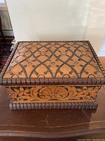 Front and top view of rectangular wooden box showing the carved geometric lattice design on the lid.