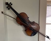 Violin mounted on wall with bow resting against it, showing overall condition and display setup.