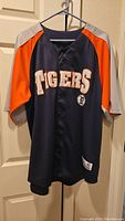 Front view of the navy blue Detroit Tigers jersey with orange and gray sleeves, "TIGERS" on chest.