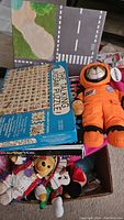 Box containing Talking U.S.A. puzzle, orange astronaut plush doll, road play mat, and other toys.