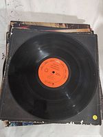 Photo of vinyl record resting on worn album covers with visible damage and edge wear.