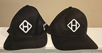 Front view of two black snapback hats with white diamond H logos embroidered