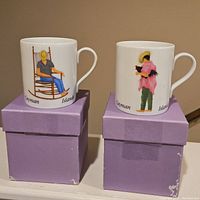 Pair of white porcelain mugs with Cayman Islands themed illustrations placed on purple boxes.