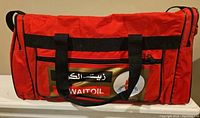Front side of a red duffle bag displaying Kuwait Oil related graphics and black carrying handles.