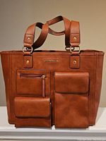 Full front view of brown leather Liz Claiborne laptop bag showing three front compartments and double handles.