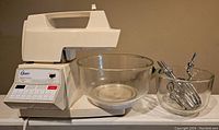 Front view of vintage Oster Kitchen Center mixer with large and small glass bowls and metal beaters attachments placed in front.