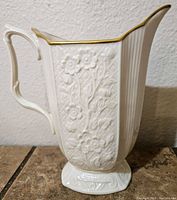 Side view of the ivory porcelain pitcher showing embossed floral design and handle