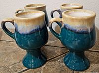 Set of four footed mugs showing overall shape, color, and condition