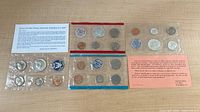 Top-down photo showing two sealed coin proof sets with various coins visible inside and informational inserts.