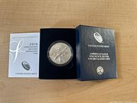 2015 American Eagle silver coin in a protective case within a navy blue display box from the United States Mint alongside the certificate of authenticity.