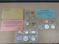 Three sealed proof sets shown with original envelopes, informational certificates, and clear plastic inner packaging revealing coins and octagonal token.
