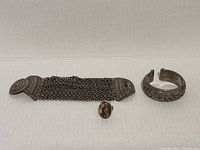 Full overview of all three jewelry items shown: wide cuff bracelet, mesh chain bracelet, and ring.