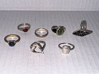 Photo showing seven rings with various stones and styles arranged on a white textured surface.