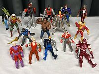 Group photo showing 13 various Marvel and wrestling action figures posed on white surface.