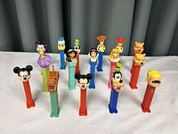 Group shot of all 14 Disney Pez dispensers together showing front profiles and varying colored bases.