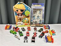 Group shot showing 18 toy items including Lalaloopsy doll, toy soldiers, and multiple miniature cars spread out on white surface