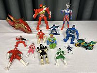 Full overview of all 12 action figures and red/gold motorcycle toy displayed on a grey surface with black background.