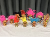Group of ten vintage Troll dolls in various hair colors and sizes arranged in two rows on white surface with dark curtain background.