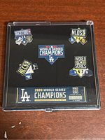 Full view of the Jim Mendel pins set showing six pins commemorating the Los Angeles Dodgers 2020 championship and playoff series victories mounted on black display backing in a clear case.