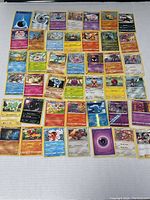 Photo showing 42 assorted Pokémon trading cards laid out on a white surface, including various types and character cards, with some holographic and special design cards visible.