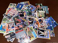 Photo showing a mixed collection of various sports trading cards spread out, featuring baseball, basketball, and football players from various sets and years.