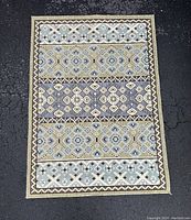 Photo of Safavieh accent rug laid flat on dark asphalt surface, showing full pattern and colors in beige and blue tones.