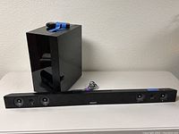 Photo of black Samsung sound bar and subwoofer placed on table with cables attached