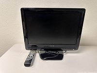 Front view of the Toshiba all-in-one TV with remote control placed beside it, showing the screen and base stand.