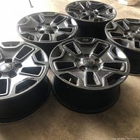 Five black Jeep rims laid on the ground showing front and side views.