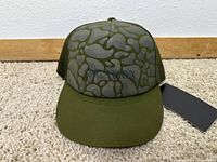Front view of olive green Arcteryx hat with patterned front and black logo embroidered.