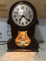 Front view of Master Crafters Bakelite mantel clock showing clock face, hands, carved details, and illuminated swinging girl figure.