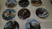 Overhead photo showing all eight collectible Paul Krapf decorative plates with wildlife animal paintings arranged flat on white cloth.