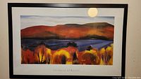Overall view of the framed print showing autumn landscape in warm colors and black frame.