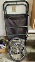 Photo of a metal frame game cart with a black fabric bag and two large wheels attached.