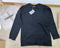 Black Gymshark oversized sweater laid flat showing front side, with original packaging bag in background.