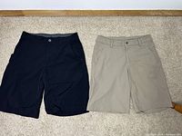 Front view of black and khaki Lululemon men's shorts laid flat showing pockets and button closures.