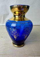 Front view of the blue and gold Murano glass vase with visible gold floral designs and rim detailing.