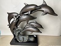 Front view showing seven dolphins leaping over wave atop wood base