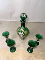 Full set of an antique Venetian green glass wine decanter with stopper and four matching wine glasses arranged on table surface.