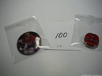 Two pins in plastic sleeves, a large circular Patrick Roy hockey pin and a smaller round Montreal Canadiens jersey pin with a handwritten '100 x2' note behind them.