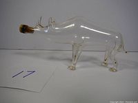 Side view of clear pig-shaped glass bottle showing four legs and cork stopper.