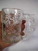 Clear glass mug displaying a detailed embossed Batman face on the front with sculpted handle held in hand for scale.
