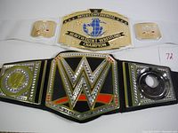 Photo showing two vintage WWE wrestling belts side by side, the Intercontinental Heavyweight Champion belt on top with white strap, and another WWE belt below with black strap.