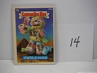 Front view of the Garbage Pail Kids "Twyla Paper" card in protective sleeve with reference number 14 beside it.