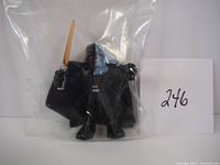 Close-up of Darth Vader figure holding light saber and wearing cape inside a clear resealable plastic bag with lot number 246 card.