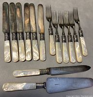 Photo showing six knives and six forks with mother of pearl handles and tarnished silver-plated blades, plus one cake cutter and one cake/cheese spreader.